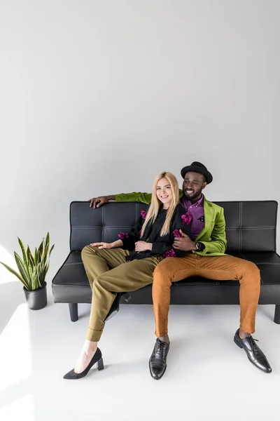 Sonriente Pareja Multicultural Moda Descansando Sofá Negro Sobre Fondo Gris — Foto de Stock