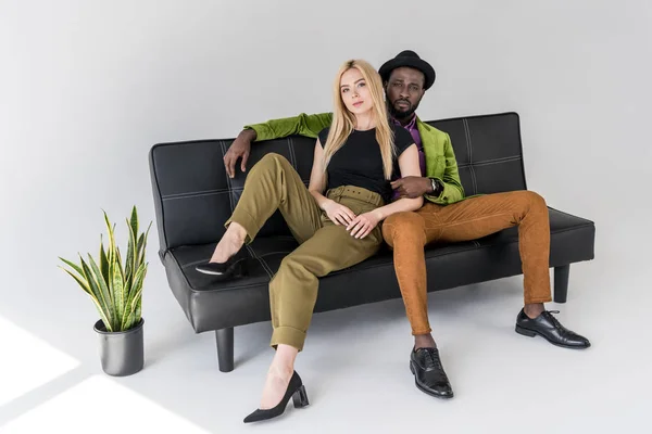 Pareja Multicultural Moda Sentado Sofá Negro Sobre Fondo Gris — Foto de stock gratis