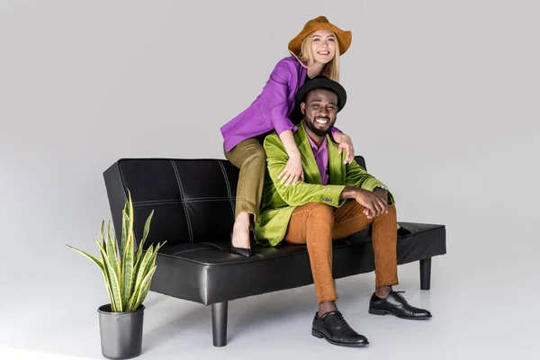 Munter Multikulturel Fashionable Par Hatte Sidder Sort Sofa Grå Baggrund – Gratis stock-foto