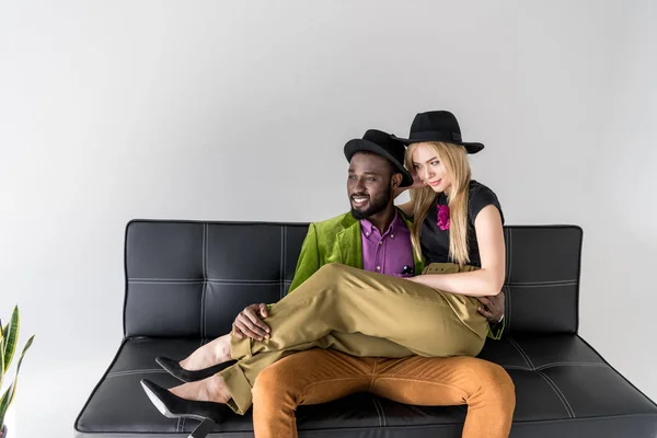 Smiling Young Multiethnic Couple Fashionable Clothes Sitting Sofa Looking Away — Free Stock Photo