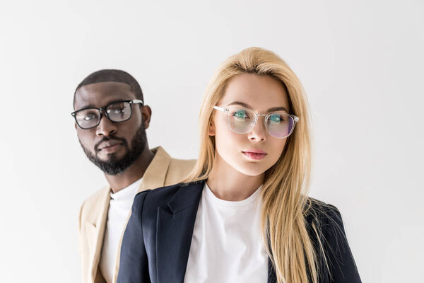 portrait of beautiful stylish young multiethnic couple in spectacles looking at camera isolated on grey