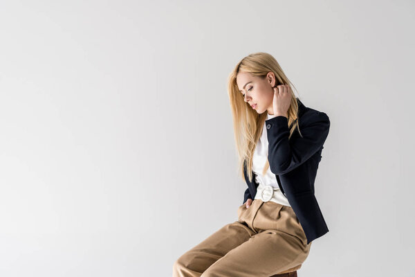 portrait of beautiful young blonde woman in fashionable clothes sitting and looking down isolated on grey 