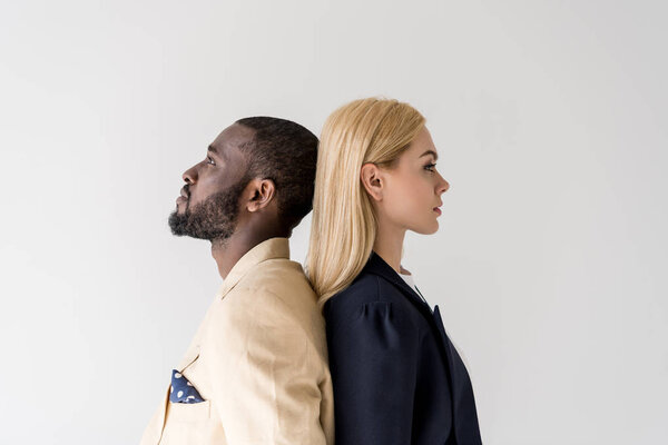side view of stylish young multiethnic couple standing back to back isolated on grey