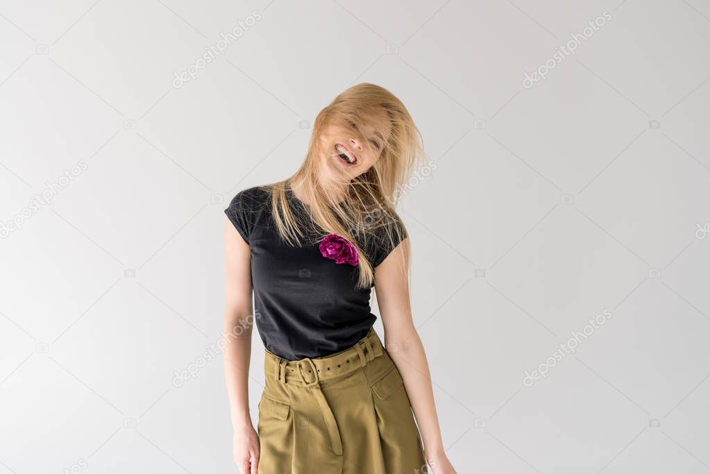 cheerful young woman shaking hair and laughing isolated on grey 