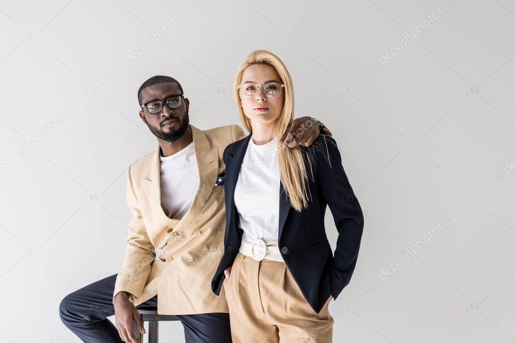 portrait of stylish young multiethnic couple in eyeglasses looking at camera isolated on grey