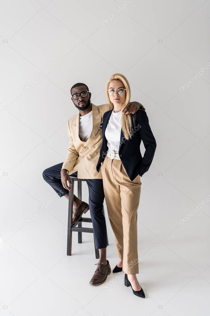 full length view of stylish young multiethnic couple in spectacles looking at camera isolated on grey