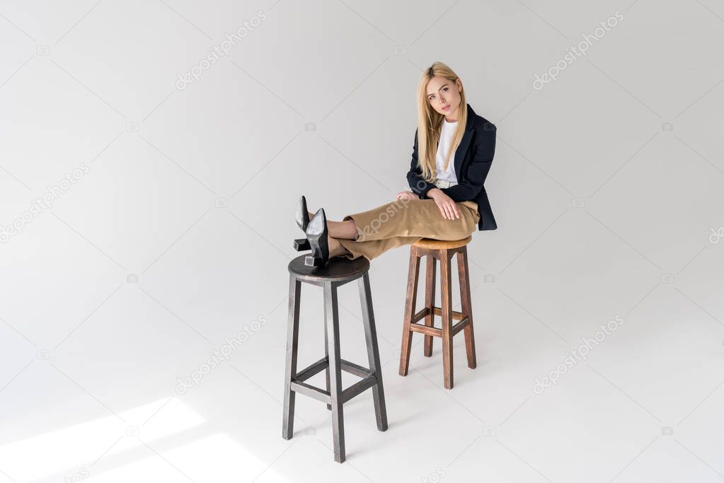beautiful stylish young woman sitting on stools and looking at camera on grey 