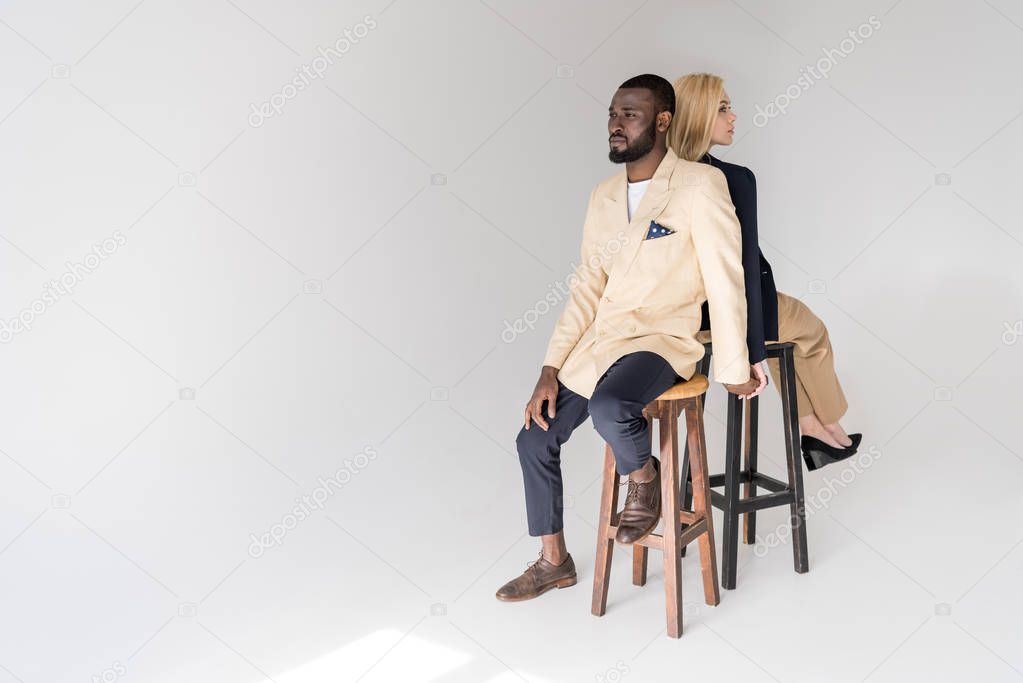 high angle view of fashionable young multiethnic couple sitting back to back on grey