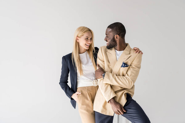happy young stylish multiethnic couple smiling each other isolated on grey