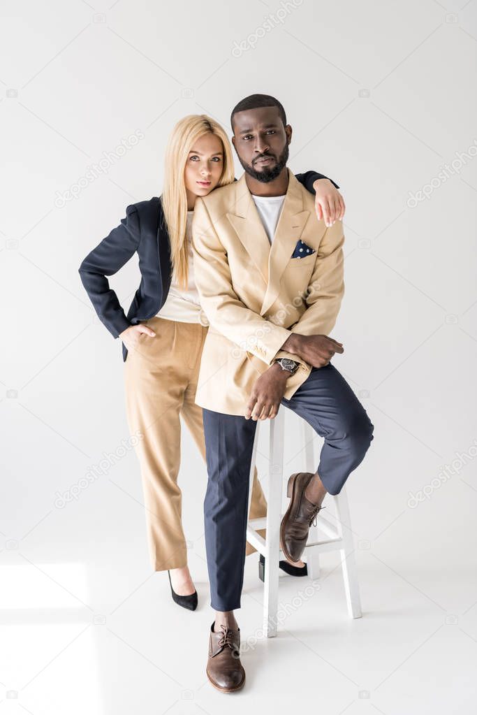 full length view of fashionable beautiful multiethnic couple looking at camera on grey 