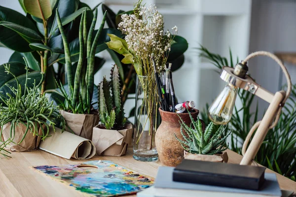 Plantas verdes con suministros de arte en la mesa - foto de stock
