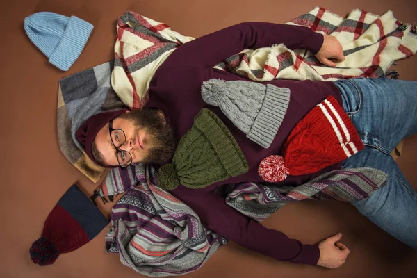 Man lying on blankets covered by hats — Stock Photo