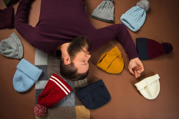 Man lying between scattered hats — Stock Photo