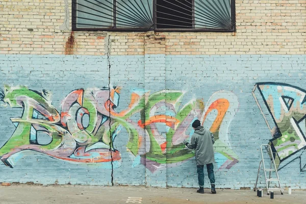 Vista trasera del hombre pintando graffiti colorido en la pared - foto de stock