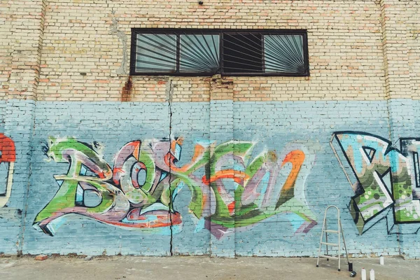 Latas con pintura en aerosol y escalera cerca de coloridos grafitis en la pared del edificio en la ciudad - foto de stock