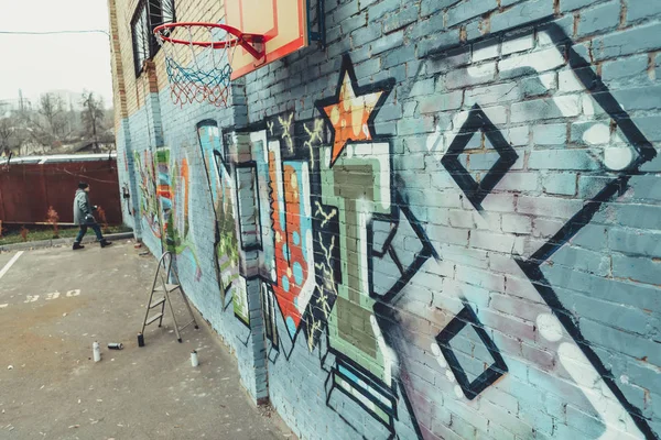 Homem pintando graffiti colorido na parede com aro de basquete — Fotografia de Stock