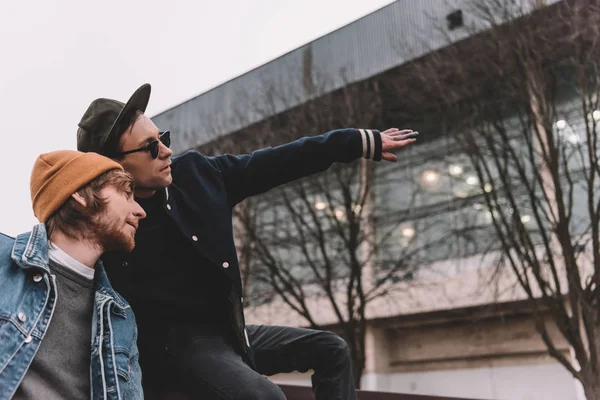 Young stylish man in sunglasses showing something to his friend — Stock Photo