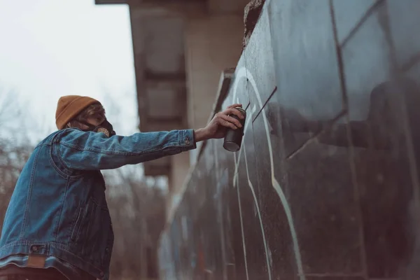 Man in respirator painting graffiti on building with can — Stock Photo