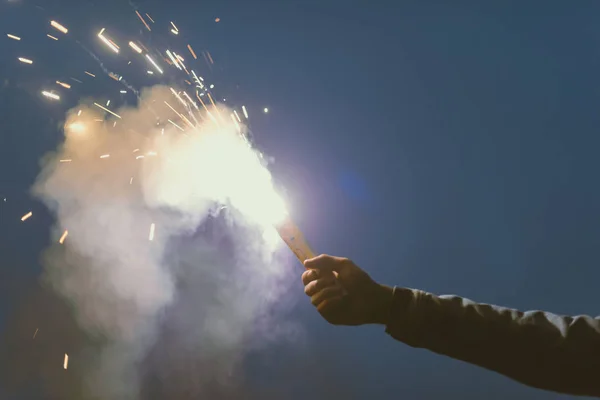 Vista cortada da mão masculina com bomba de fumaça com faíscas à noite — Fotografia de Stock