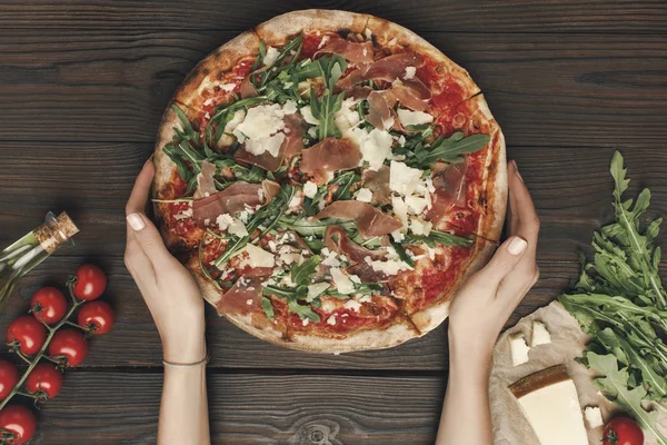 Colpo ritagliato di donna che tiene la pizza fatta in casa con ingredienti su un tavolo di legno — Foto stock