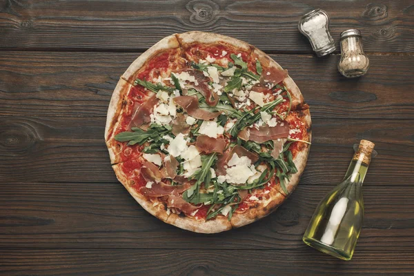 Top view of homemade pizza, olive oil and spices on wooden tabletop — Stock Photo