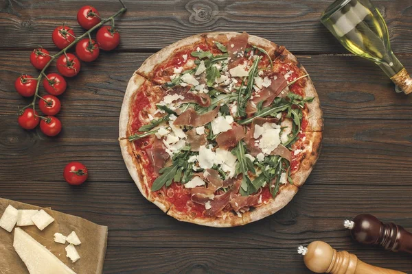 Flat lay with homemade italian pizza, olive oil, cherry tomatoes and cheese on wooden surface — Stock Photo