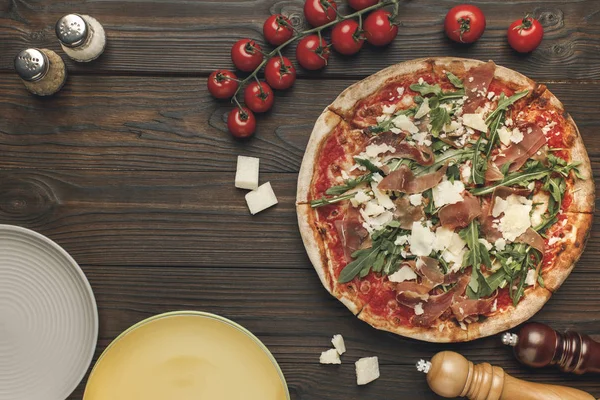 Vue de dessus de pizza italienne, tometos cerise et assiettes vides sur talbetop en bois — Photo de stock