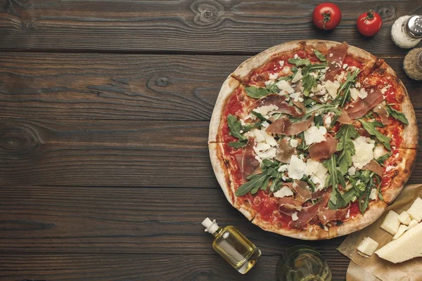 Blick von oben auf arrangierte hausgemachte italienische Pizza, Olivenöl, Kirschtomaten und Käse auf Holzoberfläche — Stockfoto