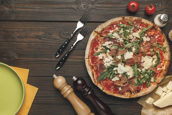 Leigos planos com pizza italiana arranjada, talheres e vários ingredientes na superfície de madeira — Fotografia de Stock