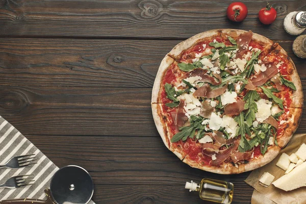 Flat lay with arranged italian pizza, cutlery and various ingredients on wooden surface — Stock Photo