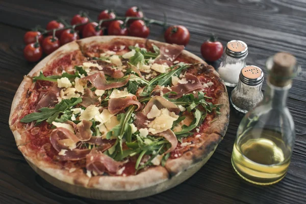 Foco seletivo de pizza italiana, tomate cereja, especiarias e azeite em mesa de madeira — Fotografia de Stock