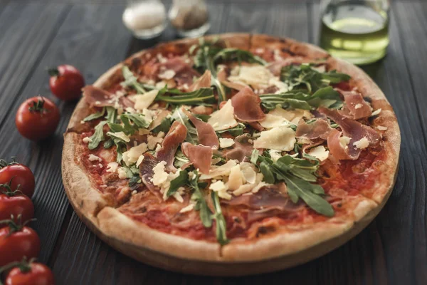 Concentration sélective des pizzas italiennes, tomates cerises, épices et huile d'olive sur table en bois — Photo de stock