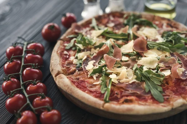 Selective focus of italian pizza, cherry tomatoes, spices and olive oil on wooden tabletop — Stock Photo