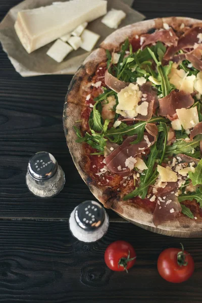 Vista de perto de pizza, especiarias e talheres na superfície de madeira escura — Fotografia de Stock