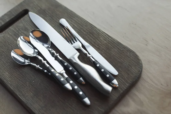 Close up view of arrangement of steel dinnerware on wooden cutting board — Stock Photo