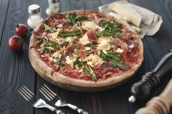Vista de cerca de pizza italiana, cubiertos e ingredientes en madera - foto de stock