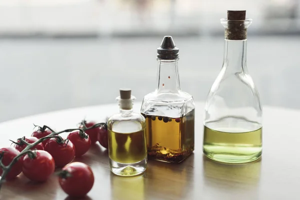 Vista de perto de vários tipos de óleo em garrafas e tomates cereja frescos — Fotografia de Stock