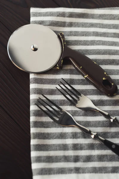 Close up view of steel forks and pizza cutter on linen napkin — Stock Photo