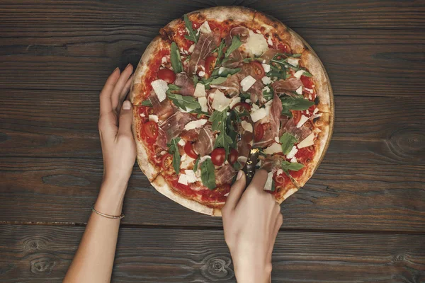 Plan recadré de femme coupant pizza italienne sur la surface en bois — Photo de stock