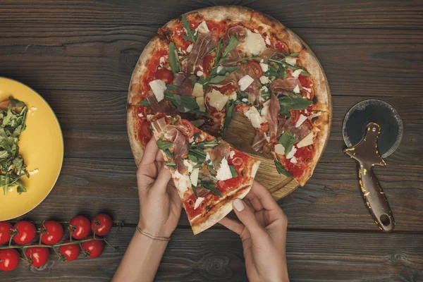 Visão parcial das mãos femininas e pizza italiana caseira na superfície de madeira — Fotografia de Stock