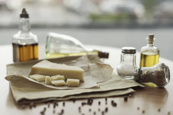 Selective focus of piece of cheese on napkin and oil in bottles — Stock Photo