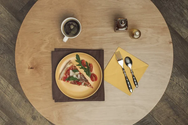 Tendido plano con pedazo arreglado de pizza en el plato, taza de té y cubiertos en la mesa de madera - foto de stock