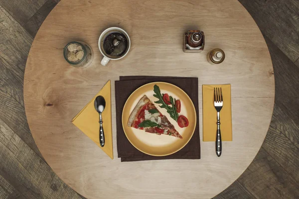 Pose plate avec morceau arrangé de pizza sur assiette, tasse de thé et couverts sur plateau en bois — Photo de stock