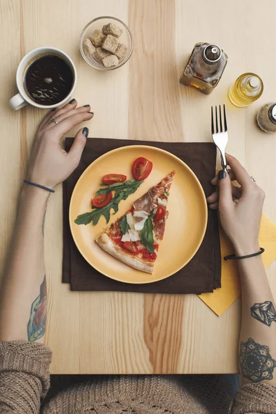 Partial view of woman sitting at table with pizza piece on plate and cup of coffee — Stock Photo