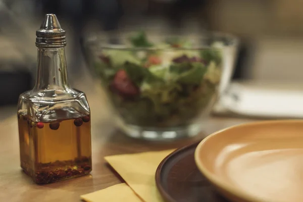 Foco seletivo de óleo em garrafa, pratos e salada em tigela na mesa — Fotografia de Stock