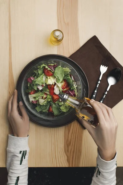 Partial view of woman pouring oil into salad at wooden table — Stock Photo