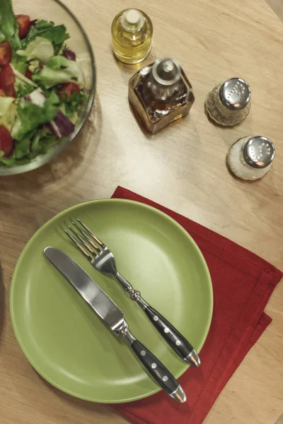 Draufsicht auf arrangierten Salat in Schüssel, Besteck, Serviette und Gewürzen auf Holzoberfläche — Stockfoto