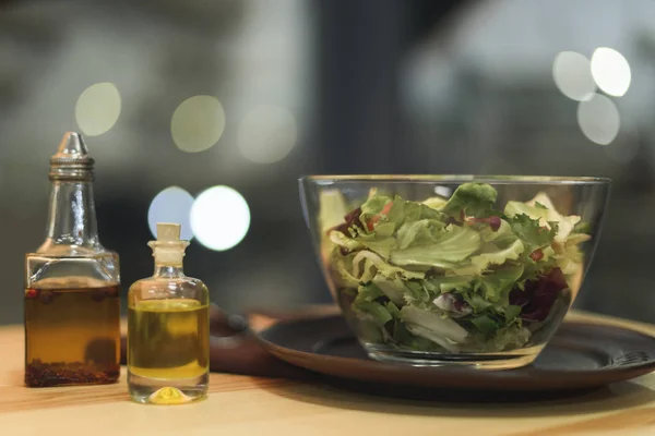 Vista ravvicinata di insalata fresca in ciotola e olio in bottiglie su superficie di legno — Foto stock