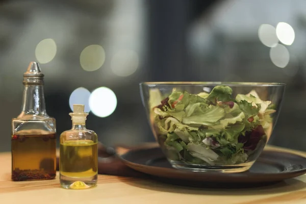 Close up view of fresh salad in bowl and oil in bottles on wooden surface — Stock Photo