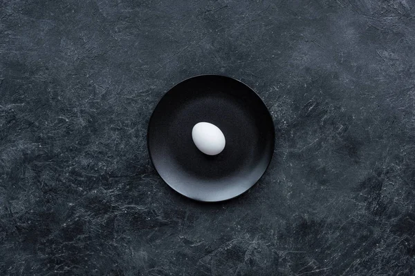 Weißes Ei auf schwarzem Teller auf dunklem Hintergrund — Stockfoto